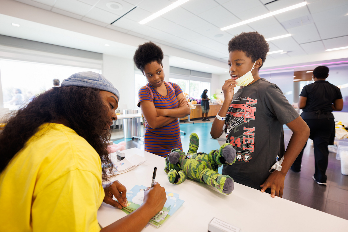 Brittany Jones, left, fills out a birth certificate for John the bear as his new owner Isaiah James, 13, and Isaiah's mother Tysierra Joseph look on during Wednesday's Furry Friends event put on by Toot, Teach and Roll.